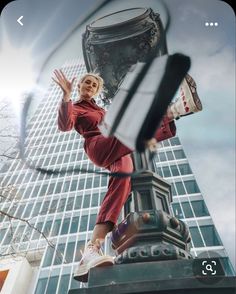 a woman standing on top of a lamp post in front of a tall glass building