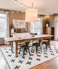 a dining room table and chairs with lights hanging from the ceiling above it, in front of windows