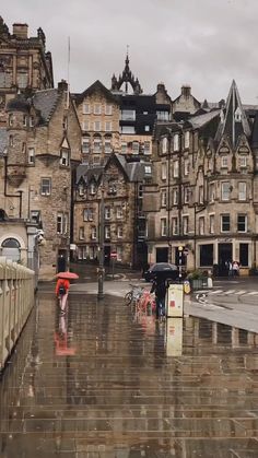 people walking in the rain with umbrellas on a city street next to tall buildings