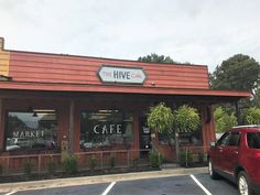 a red car parked in front of a building with the words the hive cafe on it