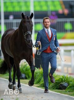 a man in a suit and tie walking a horse