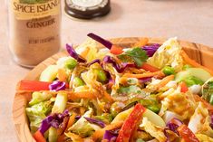 a wooden bowl filled with salad and dressing next to a bottle of spice island ginger