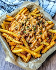 french fries covered in cheese and sauce on top of a wooden table next to a blue towel