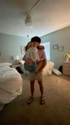 a woman holding a child in her arms while standing in front of a bedroom bed