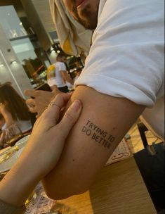 a man and woman holding hands with tattoos on their arms that say, trying to do better