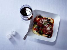 a square white plate topped with food next to a glass of wine and a salt shaker