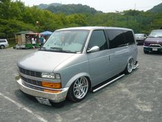 a silver van parked in a parking lot next to other cars and people standing around