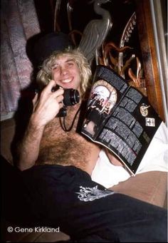 a man laying on top of a bed talking on a cell phone and holding a book