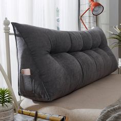 a large gray pillow sitting on top of a bed next to a lamp and potted plant