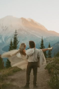 a man and woman holding each other on top of a hill with mountains in the background