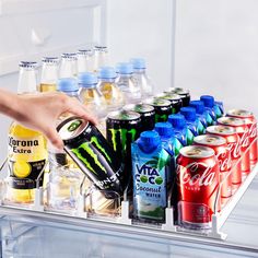 a person reaching for a can of soda in front of an open refrigerator with drinks