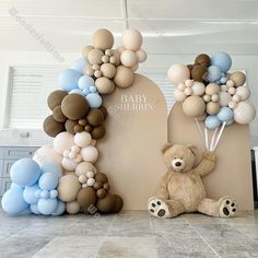 there is a teddy bear sitting next to balloons on the wall in front of it