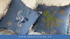 two blue pillows with an octopus and seahorse embroidered on them sitting on a bed