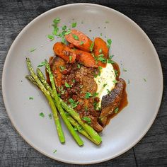 a white plate topped with meat and asparagus on top of a wooden table