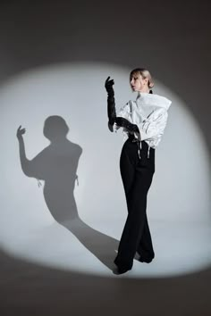 a woman in black pants and white shirt posing for a photo with her shadow on the wall