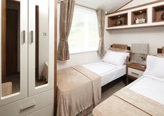 two beds in a small room with white linens and wooden shelves on the wall