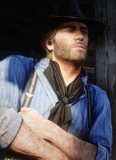 a man wearing a hat and tie standing next to a wooden wall with his arms crossed