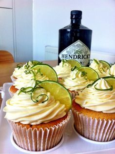 three cupcakes on a plate with lime slices and a bottle of gin in the background