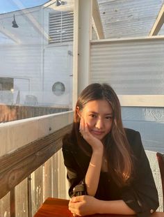 a woman sitting at a wooden table with her hand on her chin and looking off into the distance