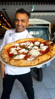 a man holding up a pizza with toppings on it