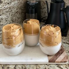 three glasses filled with liquid sitting on top of a counter next to a blender