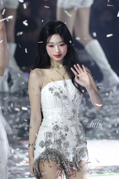 a woman in a white dress standing on a runway with confetti falling around her