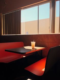 a table with a drink on it in front of a window and some red chairs