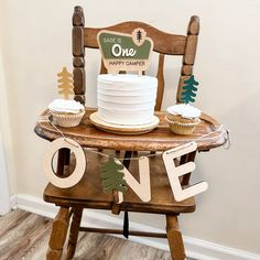 a cake and cupcakes are sitting on a wooden chair with one sign that says, same is one happy camper