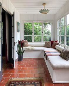 an instagram photo of a sun room with white walls and brick flooring on the bottom level