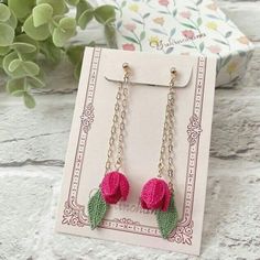 two pink crocheted flowers hanging from chain earrings on top of a white card