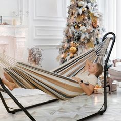 a little boy laying in a hammock next to a christmas tree and fireplace