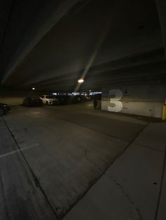 an empty parking lot at night with cars parked in the garage and people walking around