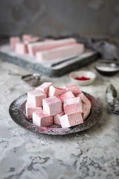 a plate full of pink and white marshmallows on a table with spoons