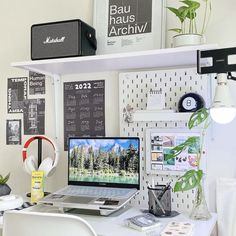 a white desk topped with a laptop computer next to a plant and speakers on top of it