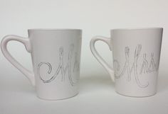 two white coffee mugs with the word mrs and mr on them, both decorated with silver thread