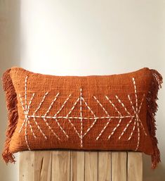 an orange pillow with white stitches and fringes on it sitting on a wooden chair