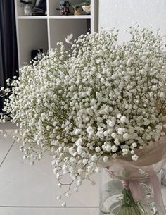 a vase filled with white flowers sitting on top of a table next to a book shelf