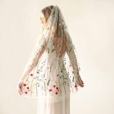 the back of a woman wearing a white veil with red flowers and leaves on it