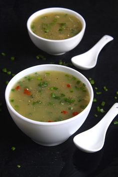 two white bowls filled with soup on top of a black table next to spoons