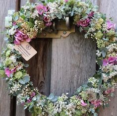 a wreath made out of flowers and leaves hanging on a wooden door with a tag attached to it