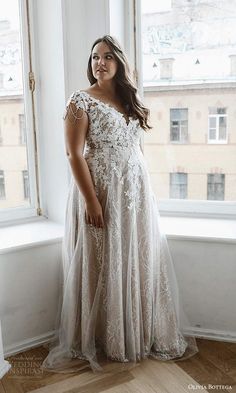 a woman standing in front of a window wearing a wedding dress and posing for the camera