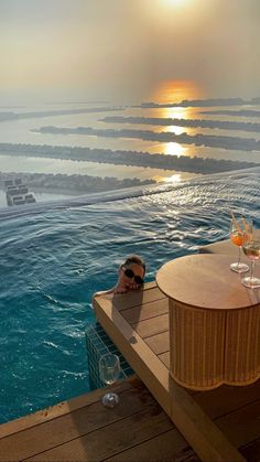 a woman laying on top of a wooden bench next to a swimming pool filled with water