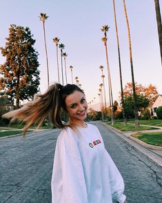 a girl with long hair walking down the street in front of palm trees and houses