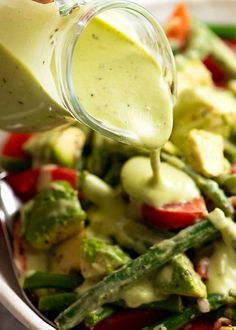 a person pouring dressing over a salad in a bowl with asparagus and tomatoes