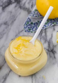 a glass jar filled with lemon custard on top of a marble table next to two lemons