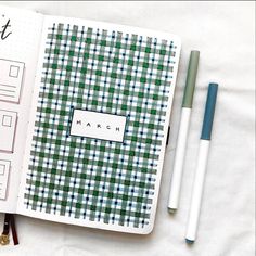 an open planner book sitting on top of a bed next to two pens and a calculator