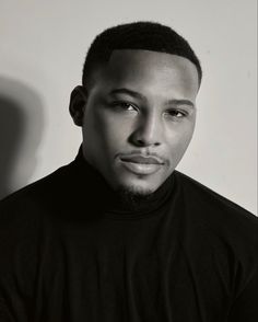 a black and white photo of a man in a turtle - neck shirt looking at the camera