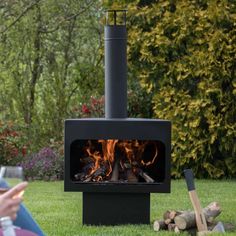 a person sitting on the grass in front of an open fire place with logs around it