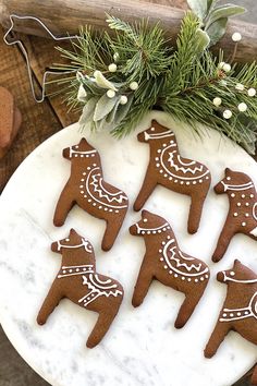 four decorated cookies sitting on top of a white marble platter next to christmas greenery