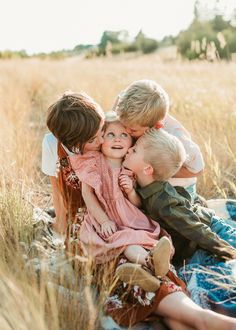 a group of children sitting on top of each other in a field with tall grass